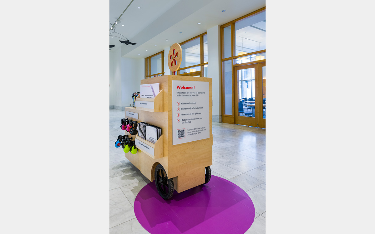 A wooden cart with accessibility resources. A sign says "Welcome" and gives instructions.