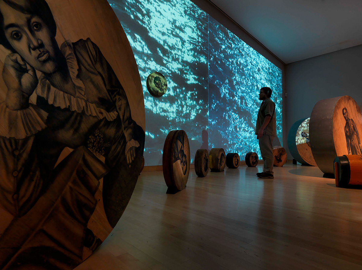 Gallery installation showing several large wooden discs, found objects, soil and video projections.