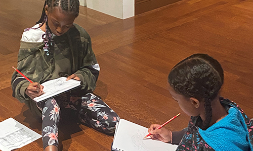 Two young Black visitors sketch in the gallery