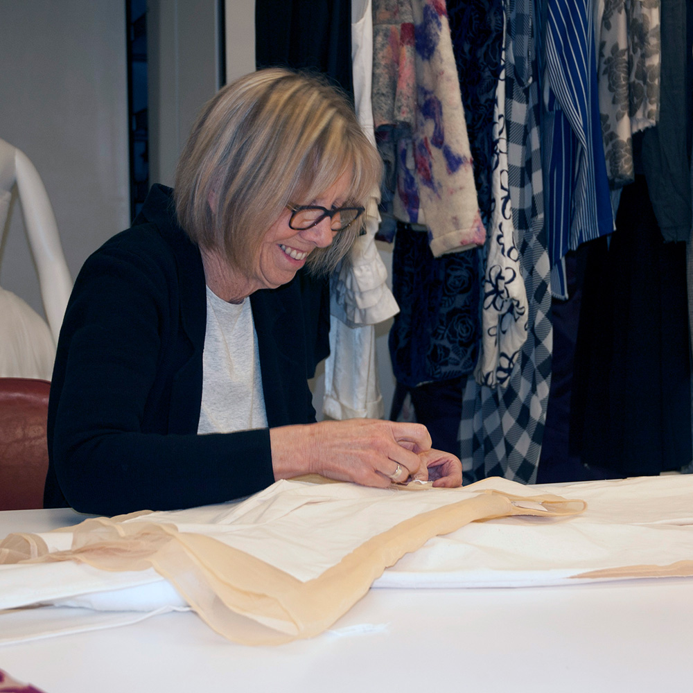 A white woman smiles while stitching a textile
