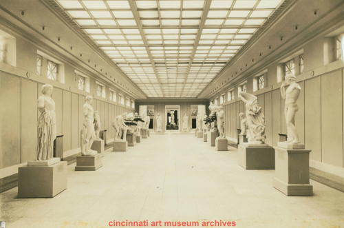 old black and white photo of a hall lined with marble statues