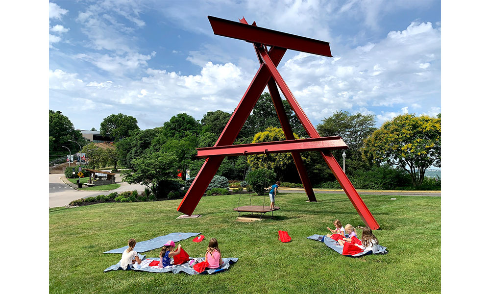 Summer Campers eating lunch outside by a big red scuplture