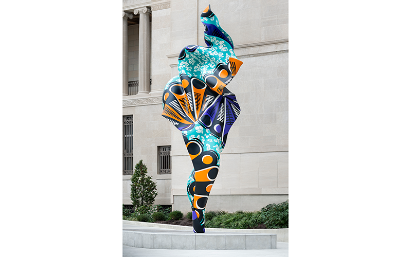 A tall sculpture that looks like a funnel, getting wider as it rises. Thes sculpture has bright orange, purple, and light blue designs on its surface.