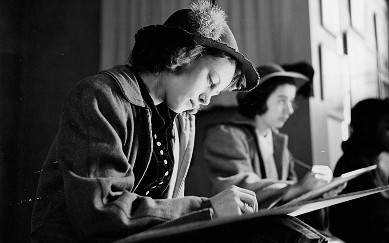 A historic black and white photo of a young woman sketching