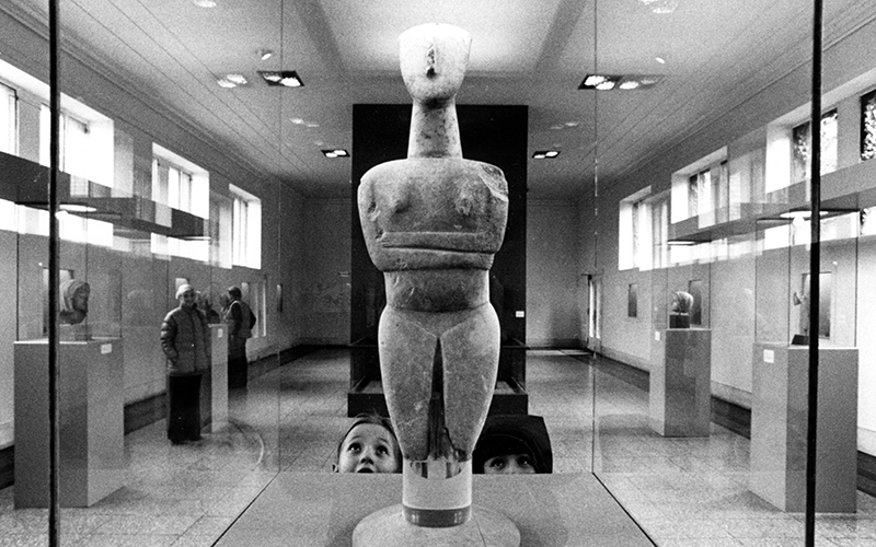 A historic black and white photo of two kids looking up at an ancient sculpture