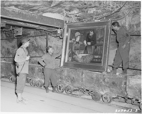 A historic black and white photo of three soldiers looking at a painting in a mine