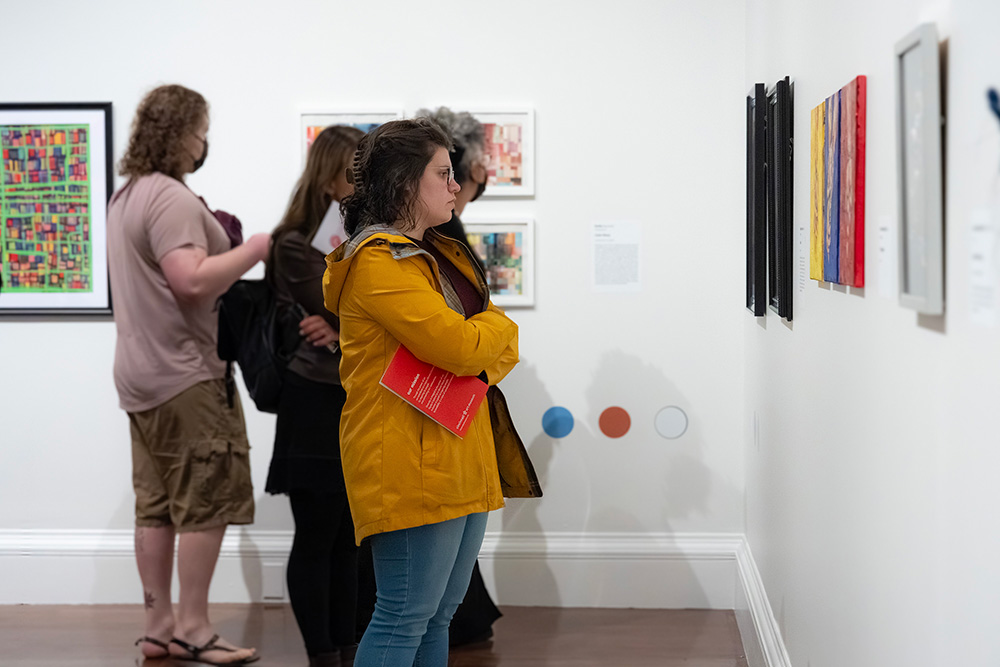 A white woman in a yellow jacket looks at framed art on the wall