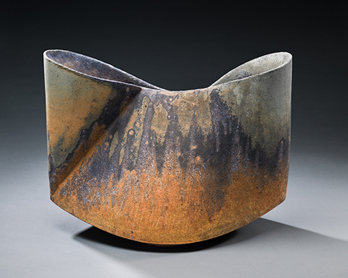 A ceramic form looking like a pinched bowl with a rough, rust-colored glaze