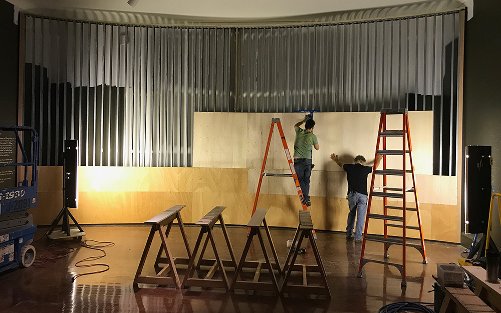 Two white men attach wood panels to a steel frame.