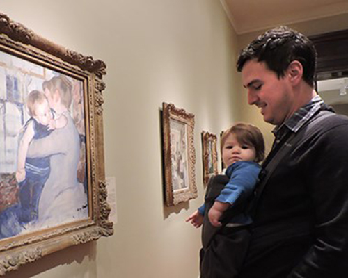 A baby in a sling and their parent enjoy an artwork