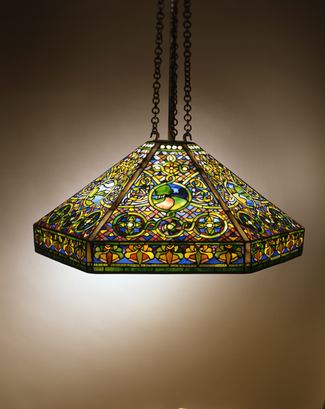 Tiffany Studios Landscape Hanging Shade, hexagonal lampshade densely decorated with colorful stained glass. In the center of each side is a circular countryside landscape