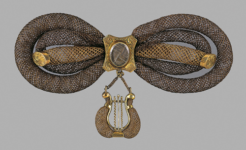 a gold brooch with coils in the shape of the infinity symbol and a harp hanging from the center
