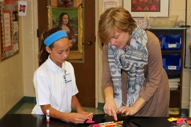 a girl watches closely while receiving instruction on an art project