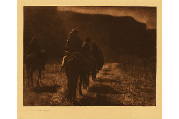 A dim, sepia toned photograph of Native Americans riding horses 