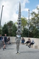 metal statue of a standing man with other human figures stacked on top, decreasing in size the higher they are
