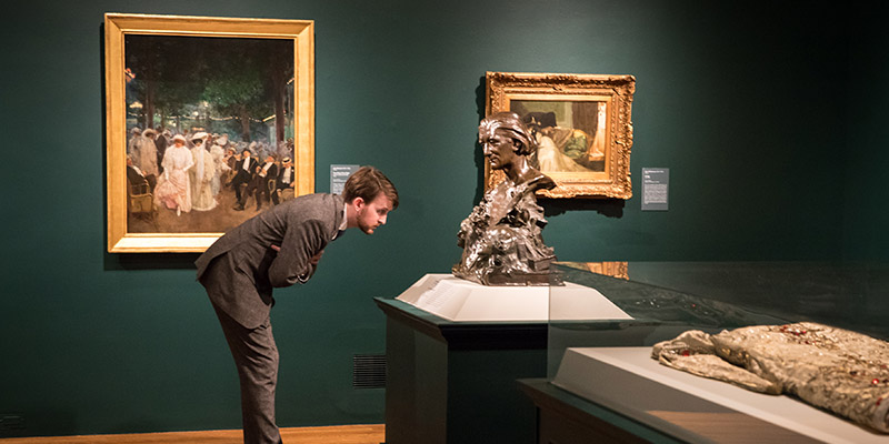 A man leans over and inspects a bronze bust inside the Paris 1900 ehibition