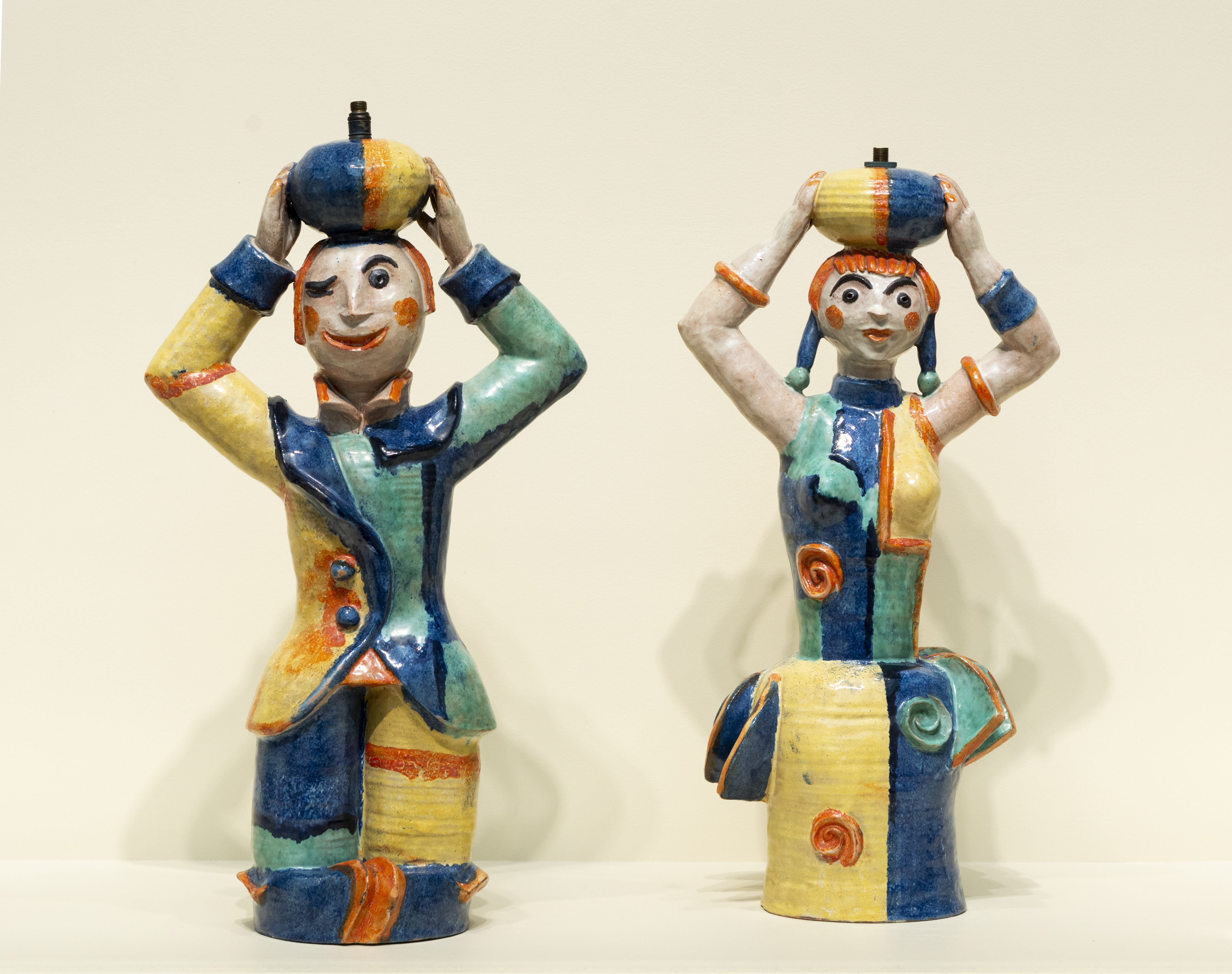 glazed lamp bases sculpted in the form of a boy and a girl wearing colorful clothing and holding baskets on their heads