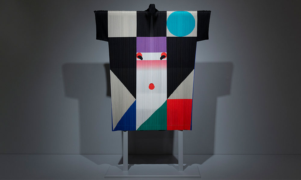 Kimono decorated with large, rigid squares and triangles of white, blue, red, and green. In the middle is a long rectangle topped with violet and decorated with a minimalist design