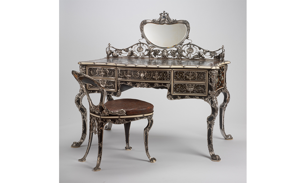 An ornately decorated writing desk with mirror and chair