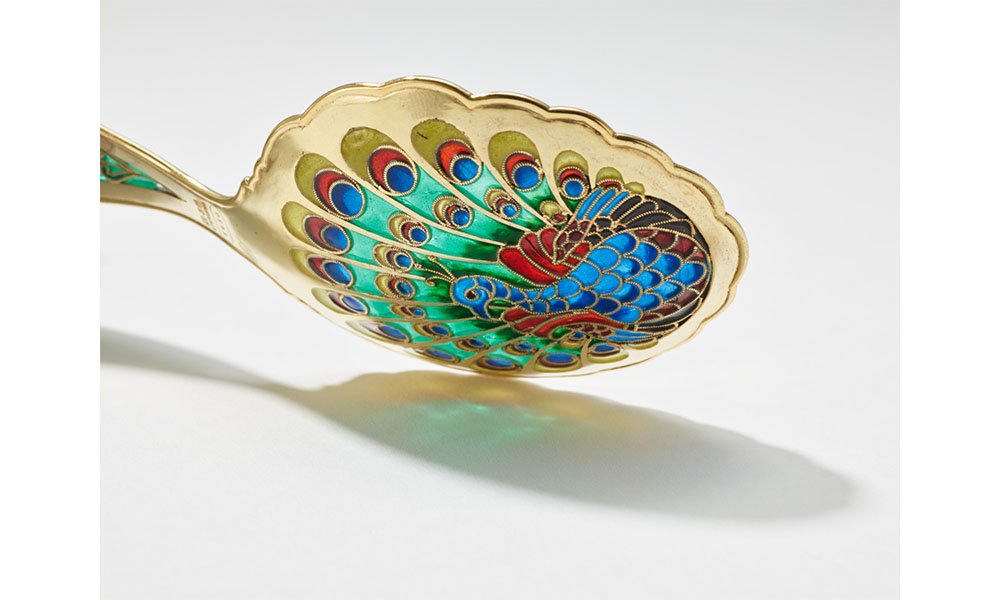 Golden spoon decorated with a colorful peacock, feathers fully extended