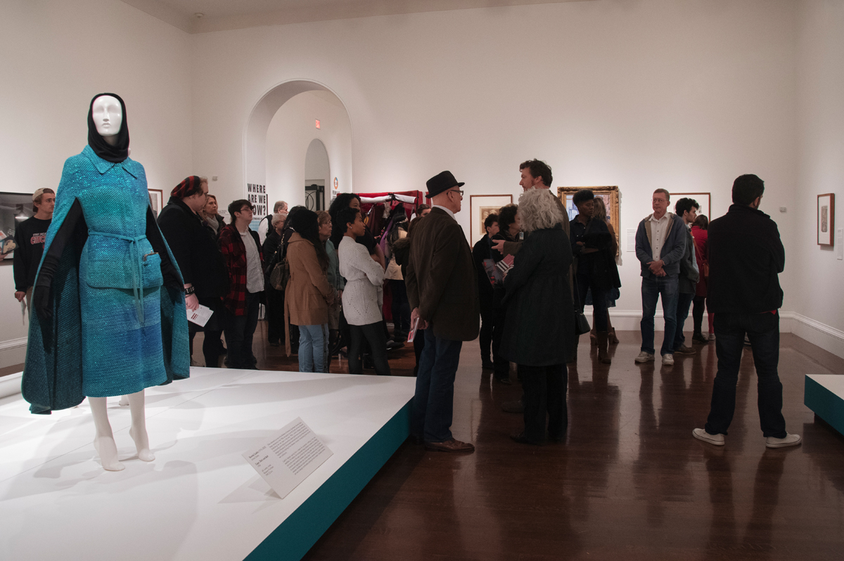 A large group of visitors mingle and admire various works in an exhibition