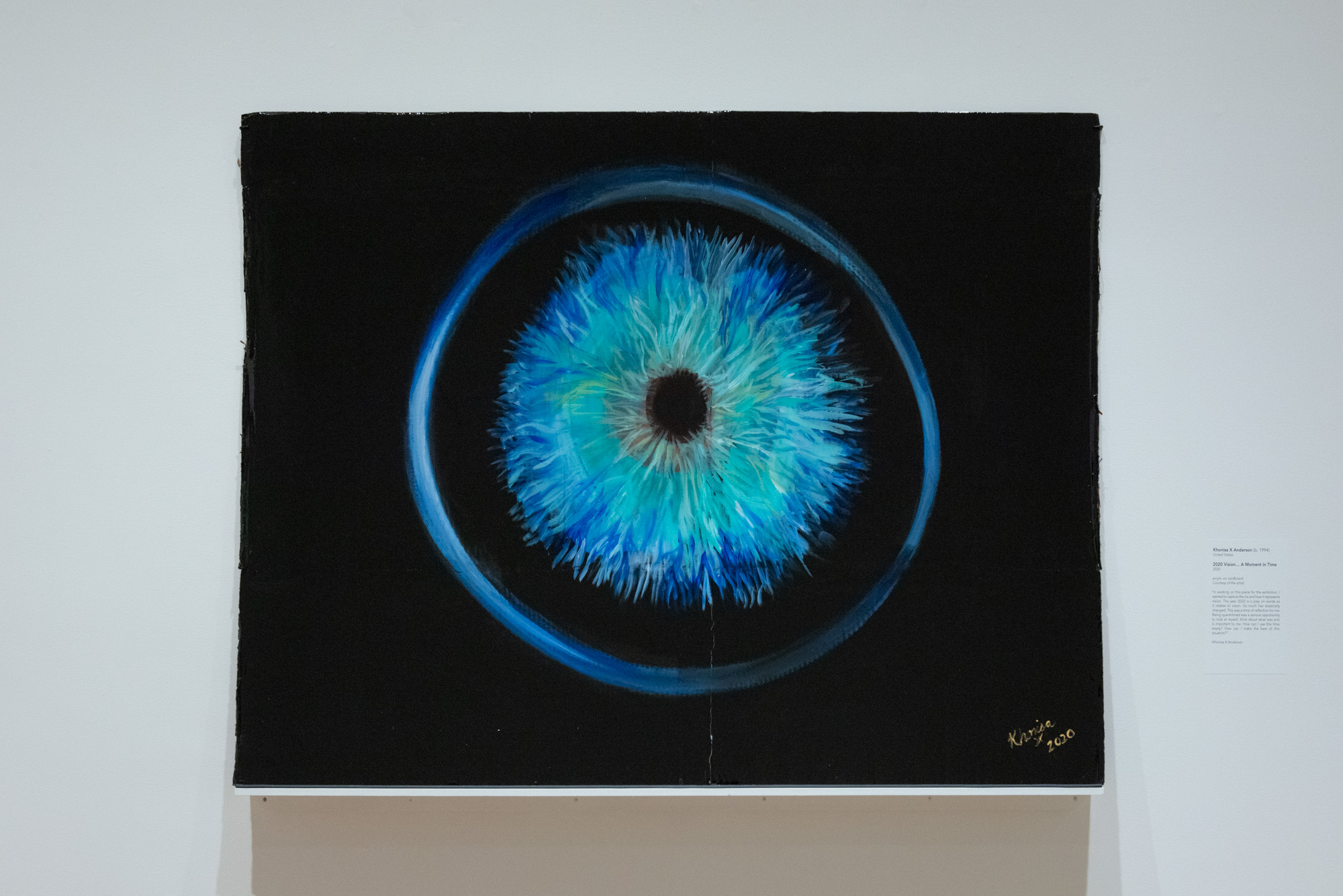 Khonisa X Anderson's 2020 Vision...A Moment In Time, a rectangular painting of a deep blue circle surrounding what seems to be an iris of blue and seafoam hues, all in a field of black. At the center is a black dot