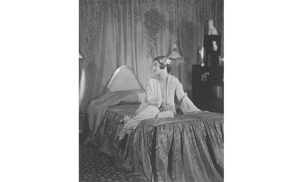 Alvina Lenke Studios' Elaine Wormser, a black and white photograph of a woman in a nightgown sitting on the bed designed by Joseph Urban, facing towards her right. 