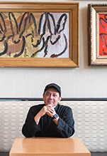 Chef Yajan (Yaj) Upadhyaya smiles while sitting at a table in the Cafe