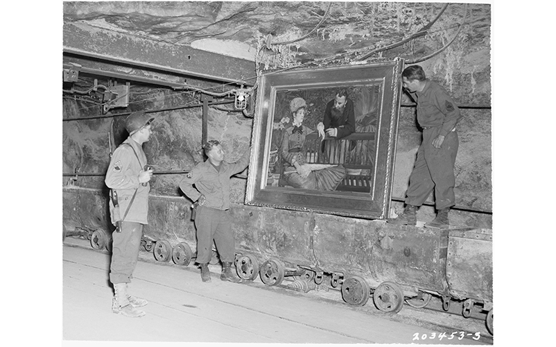 A photograph of three U.S. Army men standing in a mine shaft admiring a painting they had found