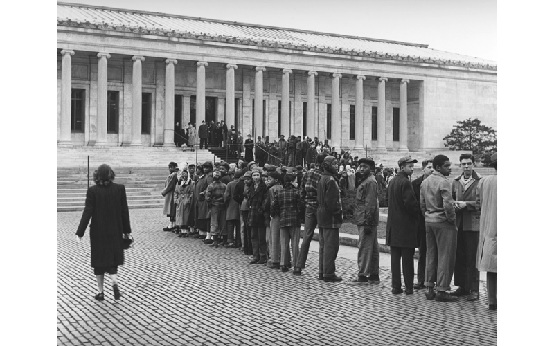 A black and white photograph of a long line of people waiting to get into the Toledo Museum