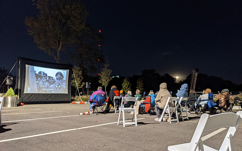 Visitors sit outside at night watching a film on a large screen