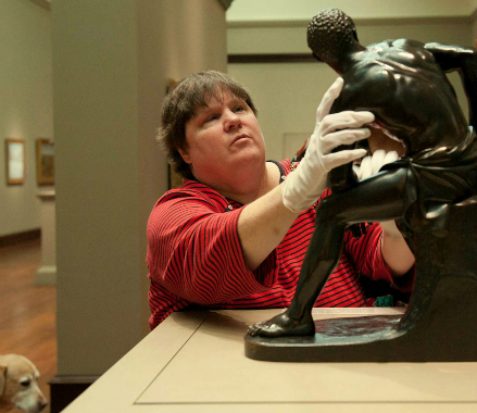 visitor on a touch tour feeling a bronze statue with latex gloves