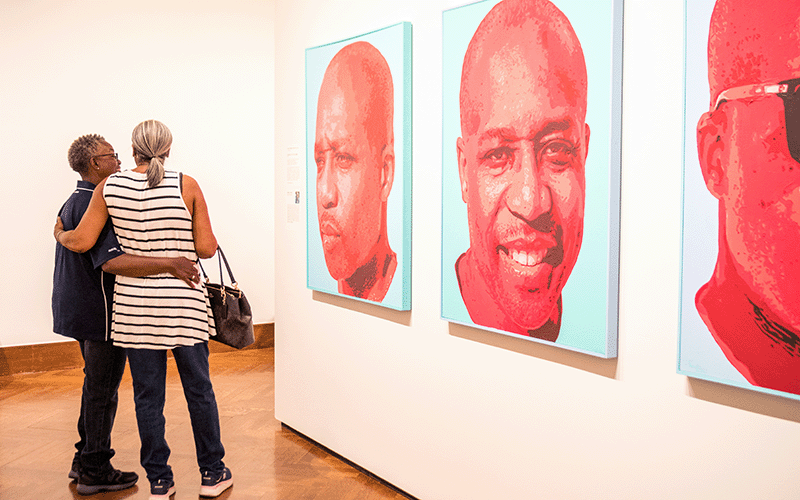 Two people embrace in front of a series of paintings