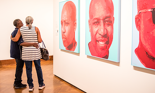 Two Black people embrace in a gallery