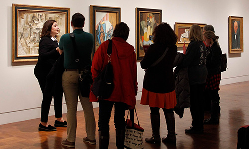 A group of adults listen to their tour guide in a museum gallery