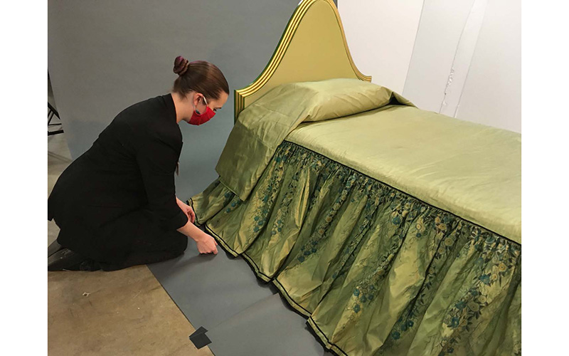 Woman adjusts the skirt of Elaine Wormser’s bedspread as it drapes over the bed.  