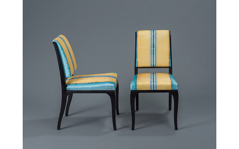 Armless chair with striped upholstery in a blue and yellow variegated striped pattern. 