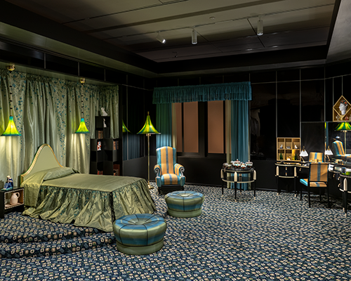 An installation view of the bedroom, featuring the green bed and intricate carpet