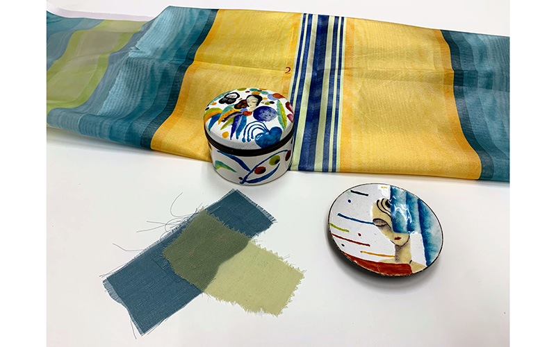 Striped yellow, green, and blue fabric samples next to a colorful lidded box and dish. 