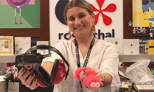 A museum staffer holds out headphones and a fidget while smiling