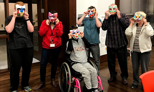 Participants hold handmade masks up to their faces for a photo