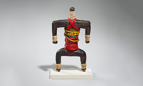 A wooden sculpture of a human figure with red and yellow bands