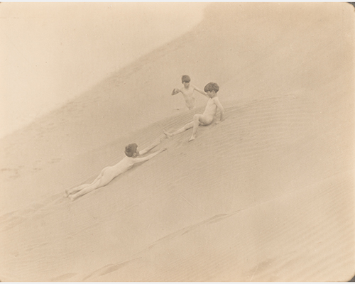 Three nude boys play in the sand