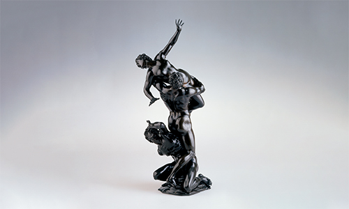 A shiny, dark sculpture featuring three struggling figures.