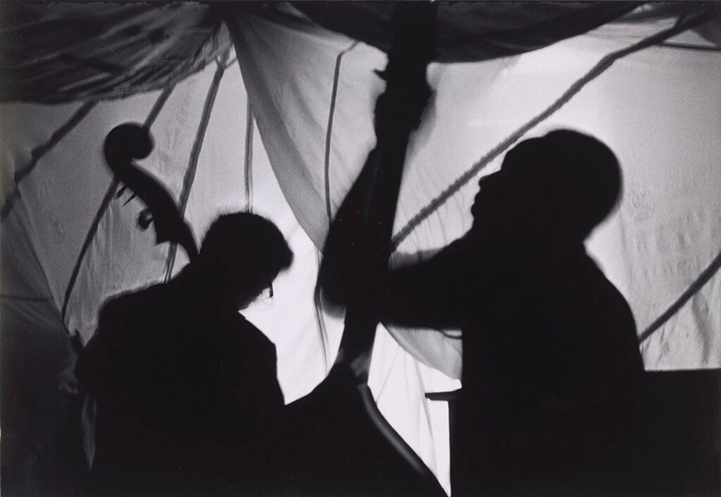 Two bass players silhouetted against bright draping fabrics