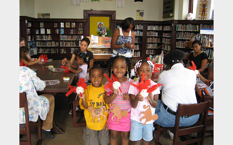 Three smiling young Black children pose with their art