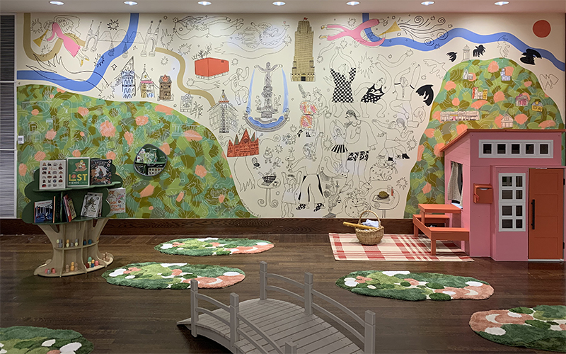 An intricate mural on a wall with a tree-shaped bookshelf and pink playhouse