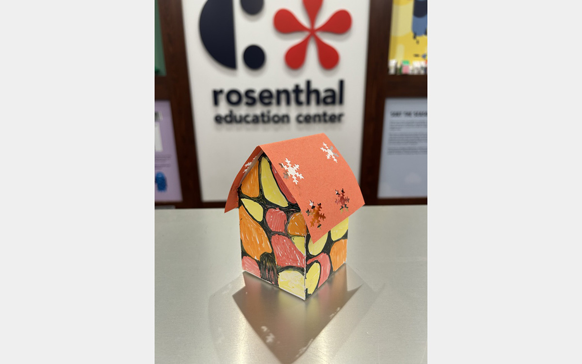 Small colorful model of a house on a tabletop with a "rosenthal education center" sign on wall in background.