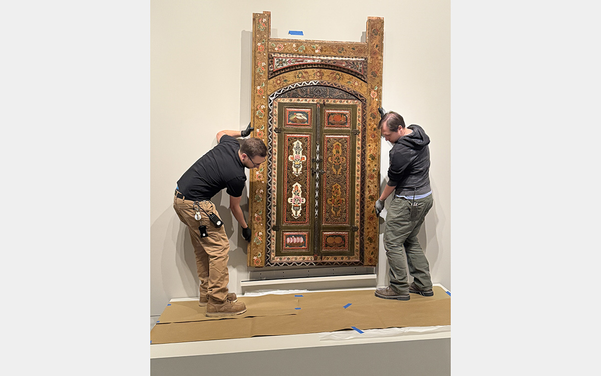 Two men lower a decorative wooden panel onto a platform.