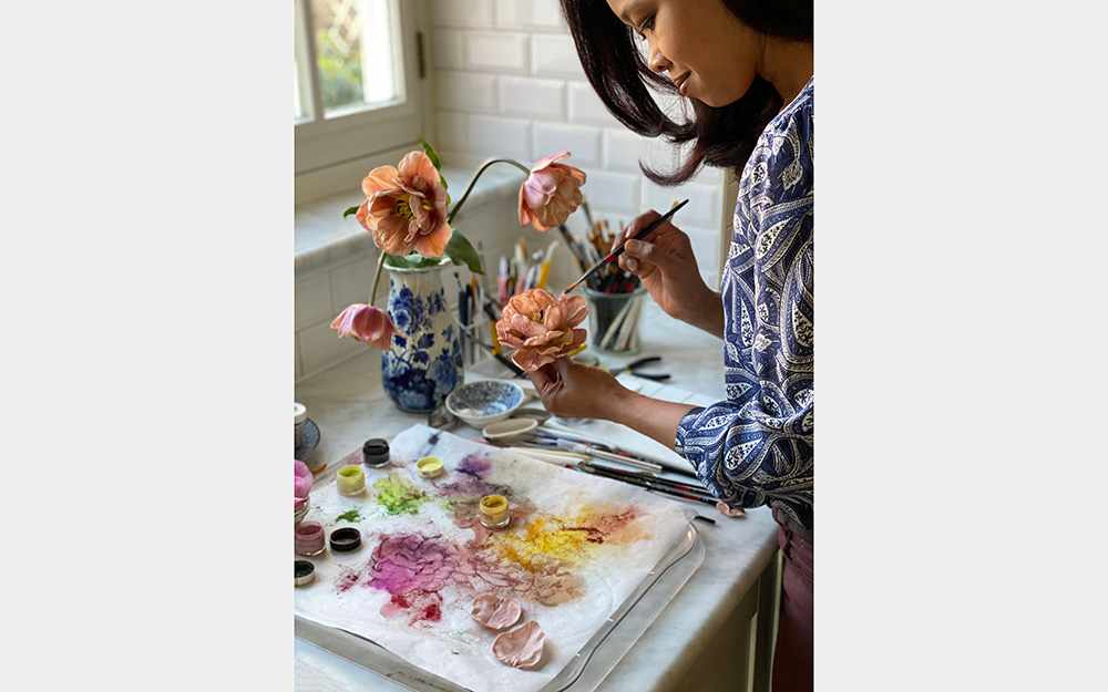 A woman paints a blossom by a window